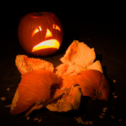 Smashed pumpkin with a pumpkin carved with a frown looking on